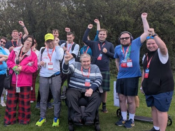 12 get2gether members at the half way point of the 2026 Kiltwalk, they are in a line looking at the camera with some member having their hands in the air in celebration, everyone is smiling.
